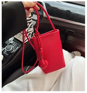 Detailed view of red pebble leather phone bag featuring woven ball strap decorations