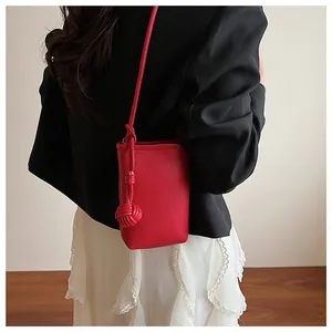 Detail of red pebbled leather mini crossbody phone bag with an elegant woven ball charm