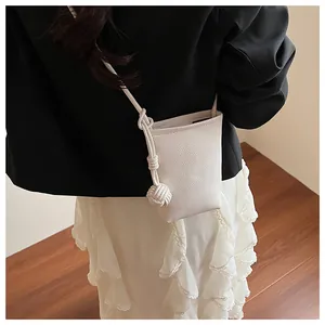 Close-up of white mini bucket bag featuring textured leather and braided knot strap
