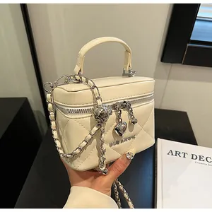 Detail der cremefarbenen Stepptasche mit Herzanhängern und Metallkettenriemen