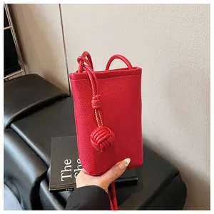 Detail of red litchi leather mini crossbody bag with unique woven knot strap decor