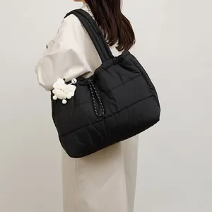 Bolso tote acolchado negro con cordón y colgante de peluche mostrado en modelo