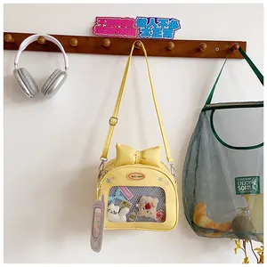 Detail of yellow Ita bag featuring transparent window with decorative plush cat and bow