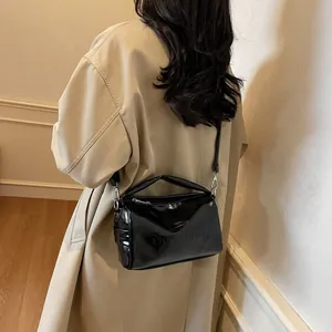 Glossy black patent leather pillow shoulder bag with embossed letters shown on model
