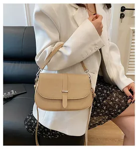 Close-up of a beige crossbody bag with flap and metal buckle on a model in a suit