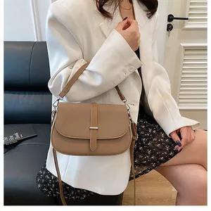 Detail of khaki textured crossbody bag with metal buckle shown on model in white blazer