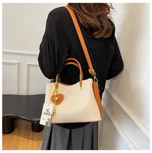 Detailed view of cream tote bag with brown trim and heart charm on a model