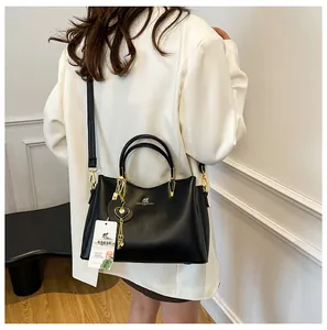 Detail of black faux leather handbag with gold hardware worn as a crossbody bag