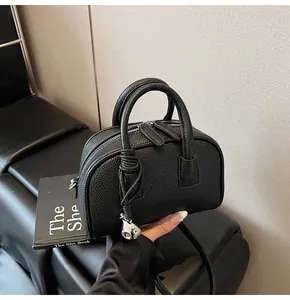 Detail of black pebbled leather handbag featuring silver charm and twin handles