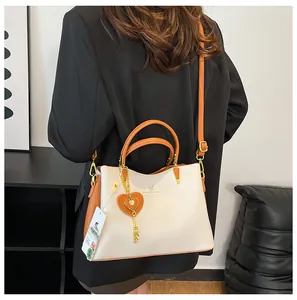 Detail view of large leather handbag with kangaroo logo and orange heart charm on model
