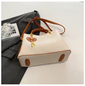 Detail of cream and brown handbag with a heart pendant and protective bottom studs