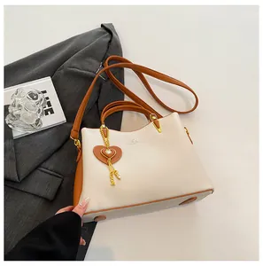 Close-up of cream and brown tote bag featuring gold heart charm and metal hardware