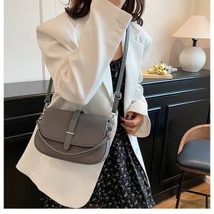 Grey saddle bag on model wearing white blazer and floral dress in soft light