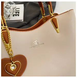 Detail of premium bicolor leather handbag with golden logo and heart-shaped pendant charm