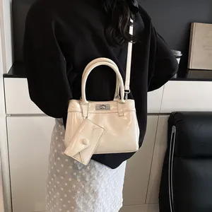 Sac à main minimaliste en cuir verni beige avec breloque assortie porté par mannequin