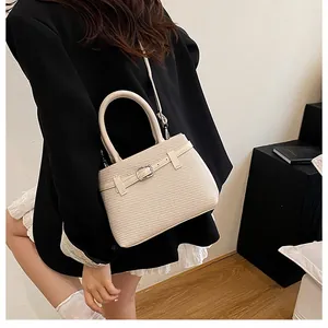 Detail of cream woven handbag with leather buckle strap and adjustable shoulder strap