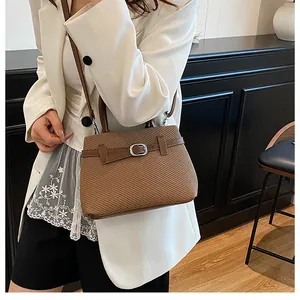 Detail of a brown woven handbag featuring faux leather straps and silver metal buckles