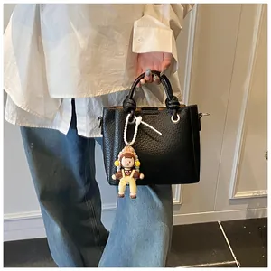 Detalle de bolso cubo de cuero granulado negro con asas anudadas y un colgante de muñeca lindo