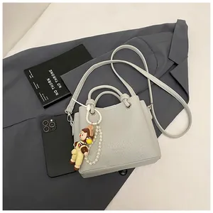 Detalle de bolso cubo gris claro con grano de lichi y colgante de perlas en chaqueta