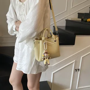 Bolso tipo cubo amarillo pálido con textura lichi y colgante de dibujo animado