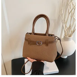 Close-up of brown woven handbag featuring faux leather straps and metal buckle detail