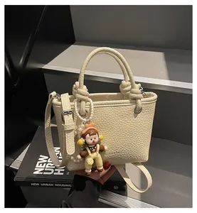 Detail of cream pebbled leather handbag with knot handles and cute doll charm