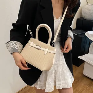 Beige woven handbag with white leather trim and top handle in a minimalist indoor setting