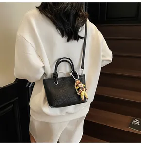Close-up of black lychee leather handbag with cute cartoon charm on a white outfit