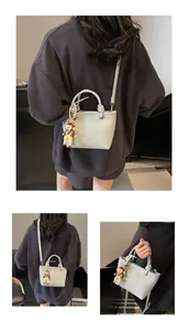Detail of light grey leather bucket bag with litchi texture and cute cartoon pendant