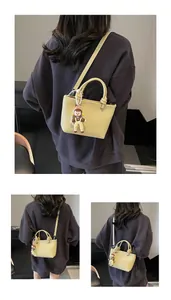 Detail of light yellow lychee pattern leather tote bag with cute cartoon doll charm