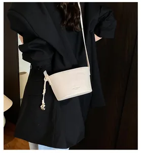 Détail du sac seau crème avec texture lychee, nœuds latéraux et pendentif argenté