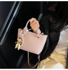 Detail of pink lychee pattern mini bag featuring knot handle and cartoon doll pendant