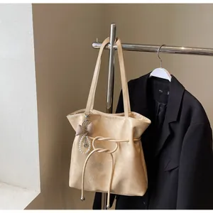 Détail du sac cabas beige avec cuir plissé, breloque nœud et nœud décoratif élégant