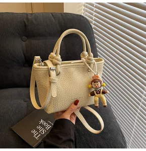 Detail of cream beige lychee pattern leather handbag with cute doll charm and strap
