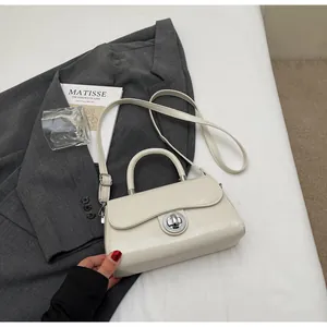 Close-up of cream leather crossbody bag with metallic circular twist-lock on a blazer