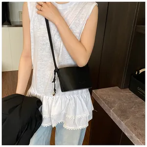 Détail d'un sac seau noir en cuir avec pendentif doré et bandoulière à nœuds élégante