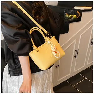 Detail of bright yellow leather bucket bag with cute bunny charm and pearl chain