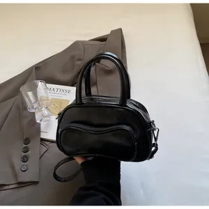 Detail of black glossy handbag featuring a unique wavy front pocket and sleek handles