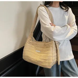 Detail of beige pleated shoulder bag featuring wavy quilted texture and silver metal tag