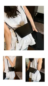 Détail du sac seau en cuir litchi noir avec breloque boule dorée et bandoulière nouée