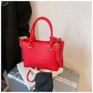 Close-up of red tote bag with lychee texture, gold hardware, and knotted handle detail