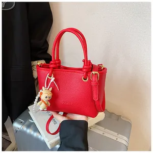 Detail view of red lychee textured leather tote bag with monkey charm on a suitcase