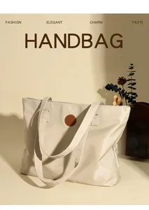 Détail du sac cabas beige avec un écusson logo en cuir marron et un design épuré