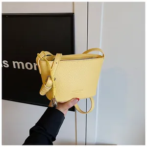 Détail du sac seau jaune texture litchi avec pendentif en métal et logo de mode