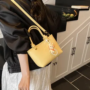 Yellow faux leather bucket bag with top handle and astronaut charm shown by model