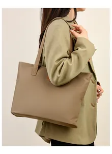 Détail d'un grand sac cabas kaki avec logo rond en cuir porté sur un blazer vert stylé