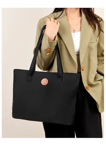 Détail du grand sac cabas noir avec logo en cuir marron et matière en nylon imperméable