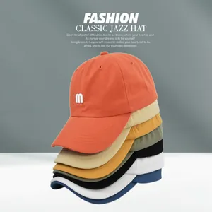 Détail de casquettes en coton empilées en plusieurs couleurs avec broderie M blanche