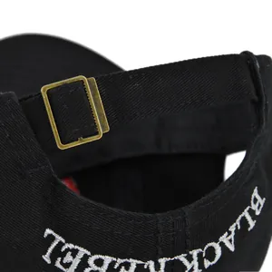 Dettaglio del berretto nero con fibbia in metallo e ricamo bianco sul retro