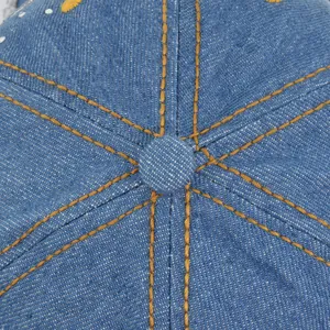 Detailed top view of denim baseball cap with yellow stitching and metal button